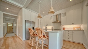 Una cocina moderna con armarios blancos, una isla central, sillas de mimbre y piso de madera.
