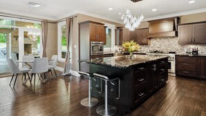 A modern kitchen with dark wood cabinets, a large island with bar stools, and a stone backsplash.