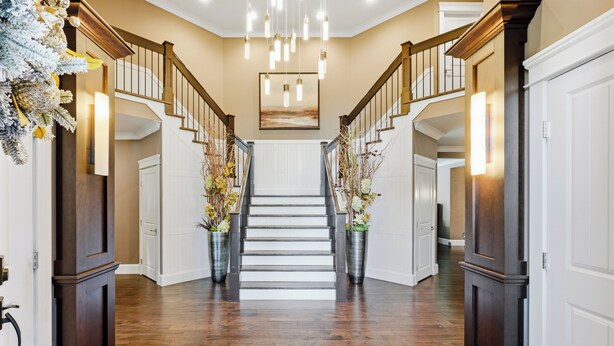 A grand staircase with a wooden finish, flanked by tall, dark wooden doors and a central white railing.