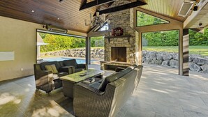 An outdoor patio with wicker furniture, a stone fireplace, and a view of a swimming pool.
