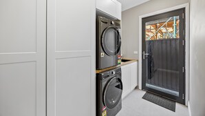 A laundry room with stacked washers and dryers, a dark door with a glass panel, and a wooden countertop. - Scott Parade Cottage (Ballarat East)