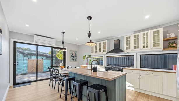 A modern kitchen with a large island, bar stools, and a view through glass doors. - Scott Parade Cottage (Ballarat East)