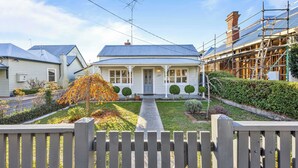 A residential house with a front porch, a pathway leading to the entrance, and a garden with trimmed bushes and a tree with autumn leaves. - Scott Parade Cottage (Ballarat East)
