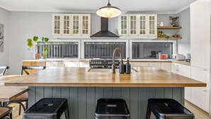 A modern kitchen with a central island, white cabinetry, and a black range hood. - Scott Parade Cottage (Ballarat East)