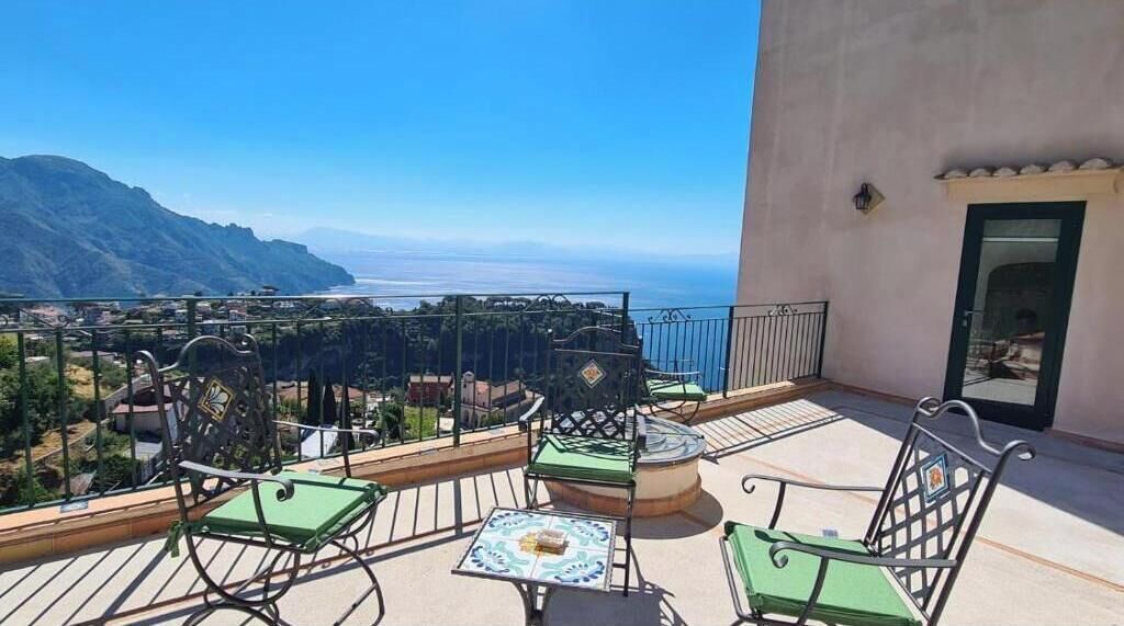 A balcony with outdoor seating, a view of the ocean, and a mountain in the background.