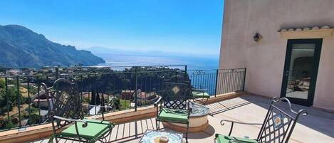 A balcony with outdoor seating, a view of the ocean, and a mountain in the background.