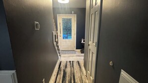 Un pasillo con una pared oscura, una puerta de color claro y un felpudo a rayas que lleva a una habitación.