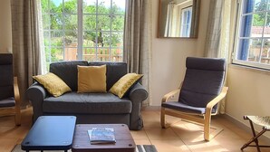 Un salon avec un canapé gris, deux fauteuils, une table basse et une fenêtre donnant sur un paysage verdoyant.