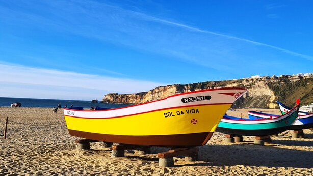 Une plage où plusieurs bateaux sont alignés, une falaise en arrière-plan et un ciel dégagé.