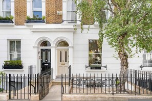 A traditional two-story building with a white facade, black iron fence, and a tree in the foreground. - Stylish Chelsea Home Amazing Location (London)