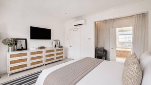 Quarto com cama, cômoda branca, TV de tela plana e janela com cortinas.