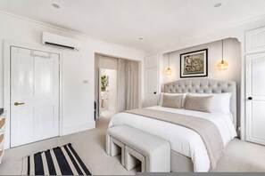 A bedroom with a large bed, a bedside table, an air conditioning unit, and a door. - Stylish Chelsea Home Amazing Location (London)