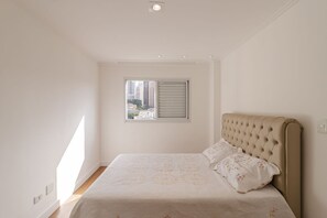 Ein Schlafzimmer mit einem Bett, einem Fenster mit Jalousien und Blick auf Gebäude.
