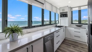 A modern kitchen with large windows, a dishwasher, and a view of the ocean. - Sunny Coast Escapes Maroochydore (Maroochydore)