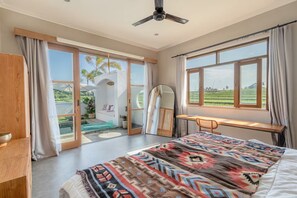 Ein Schlafzimmer mit Bett, Schreibtisch und Blick auf ein grünes Feld.
