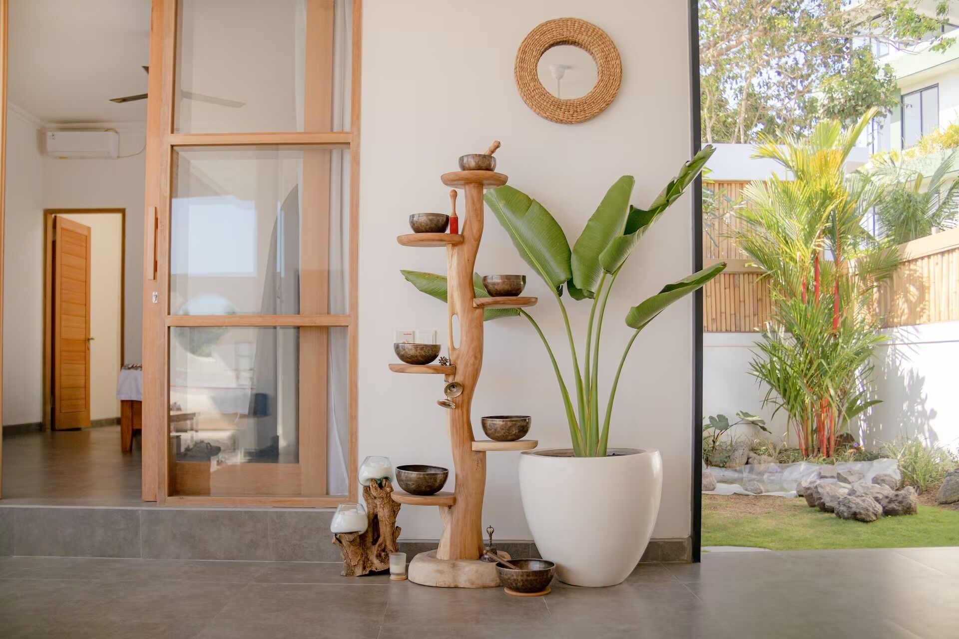 Um interior moderno com uma estante de madeira com tigelas, uma grande planta em vaso e um painel de parede tecido.