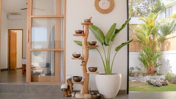 Um interior moderno com uma estante de madeira com tigelas, uma grande planta em vaso e um painel de parede tecido.