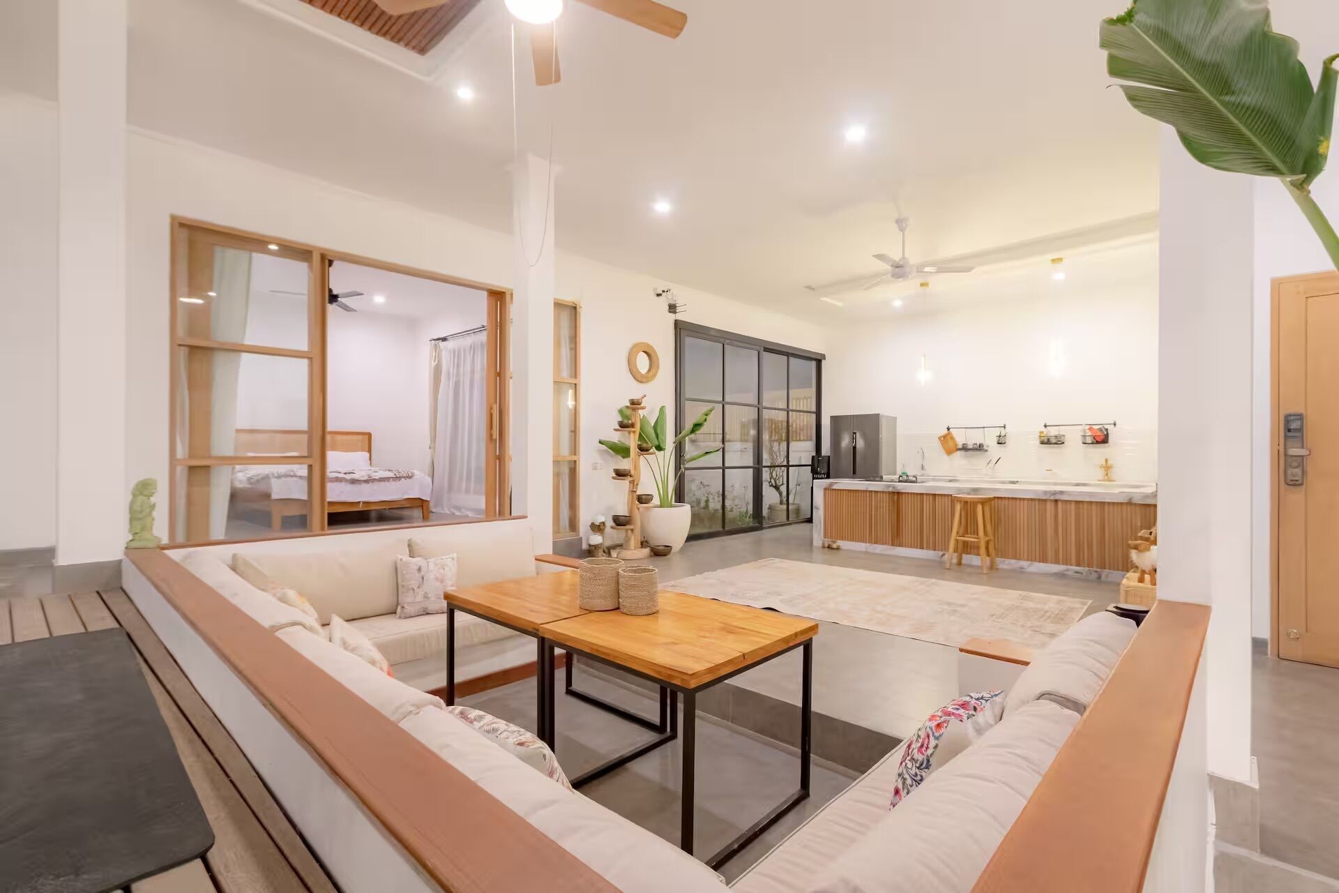 Uma sala de estar moderna com um sofá, uma mesa de madeira e uma cozinha ao fundo.