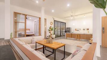 Uma sala de estar moderna com um sofá, uma mesa de madeira e uma cozinha ao fundo.