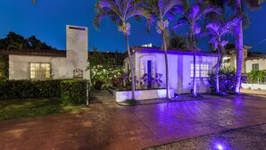 Un'area esterna ben illuminata con un vialetto lastricato, palme e un edificio con tetto in tegole.
