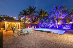 Eine Ziegelterrasse mit Swimmingpool, Palmen und einem Pavillon mit Lichterketten.