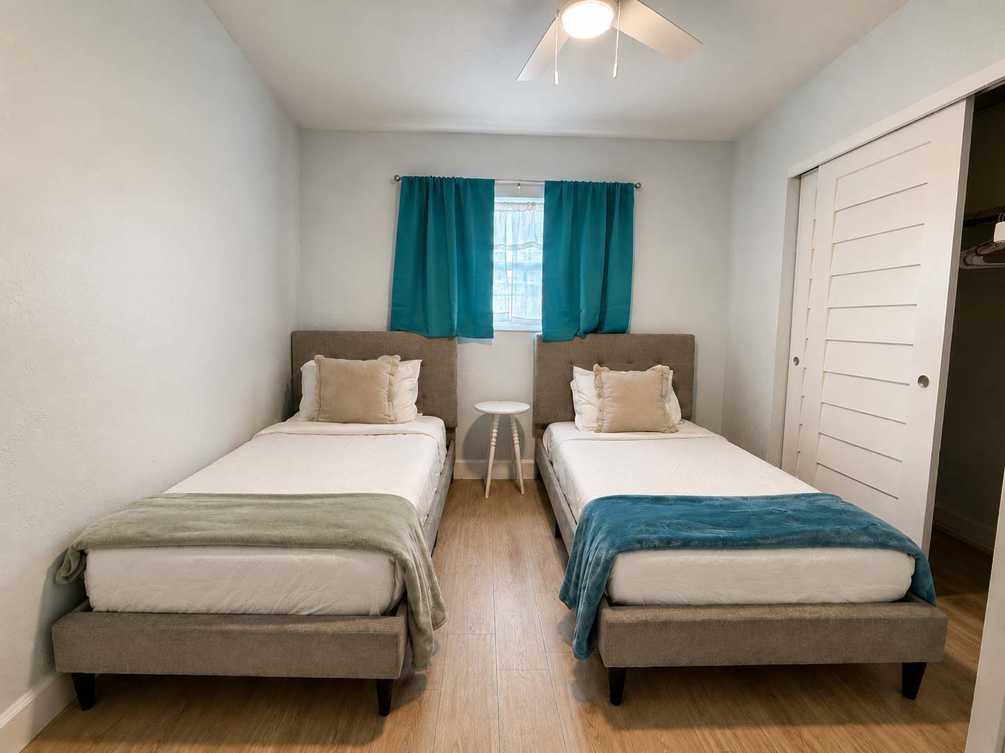 A small, clean room with two beds, a small table, and a window with curtains.