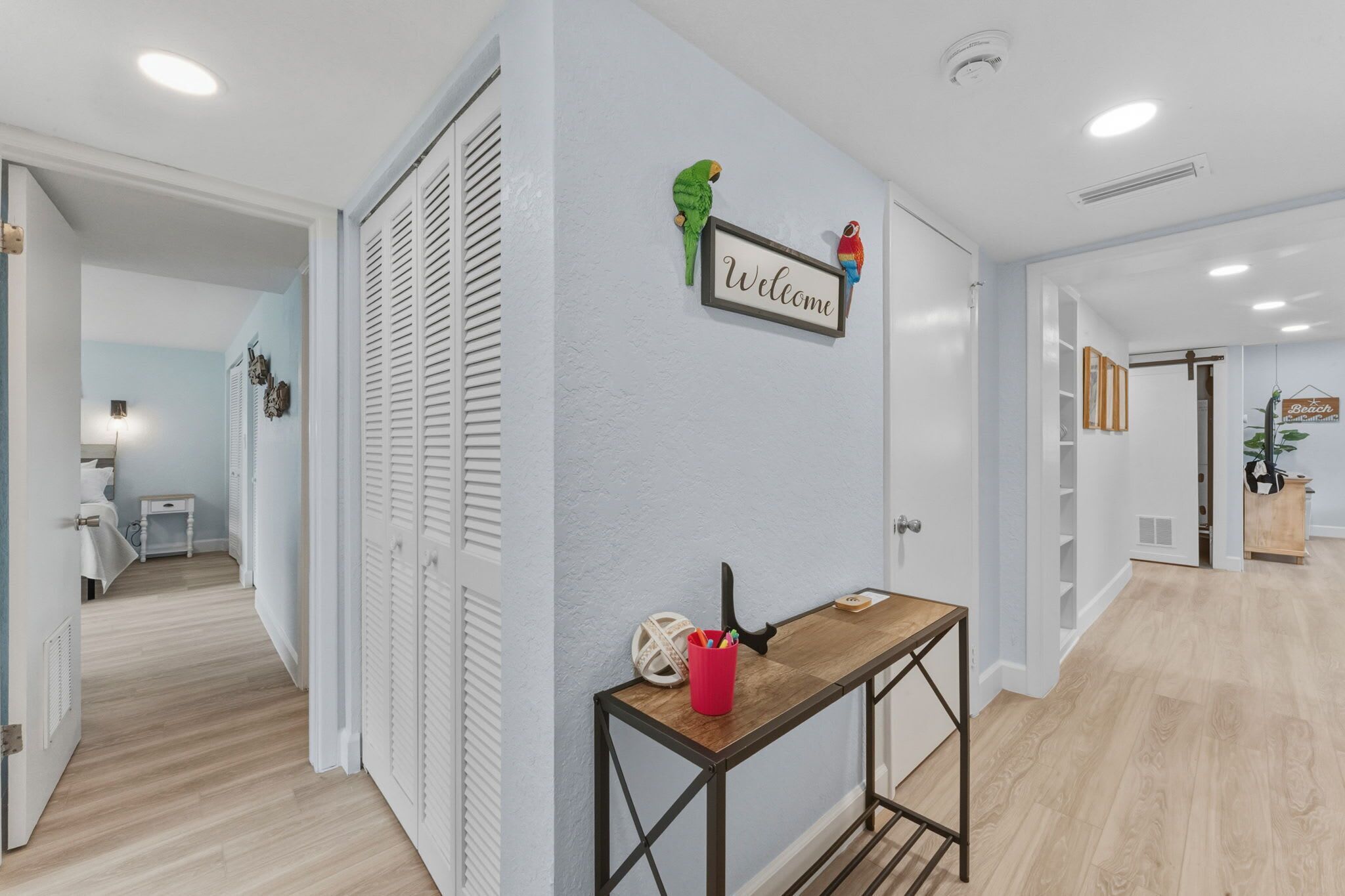 A hallway with a wooden table, a 'Welcome' sign, and a parrot decoration.