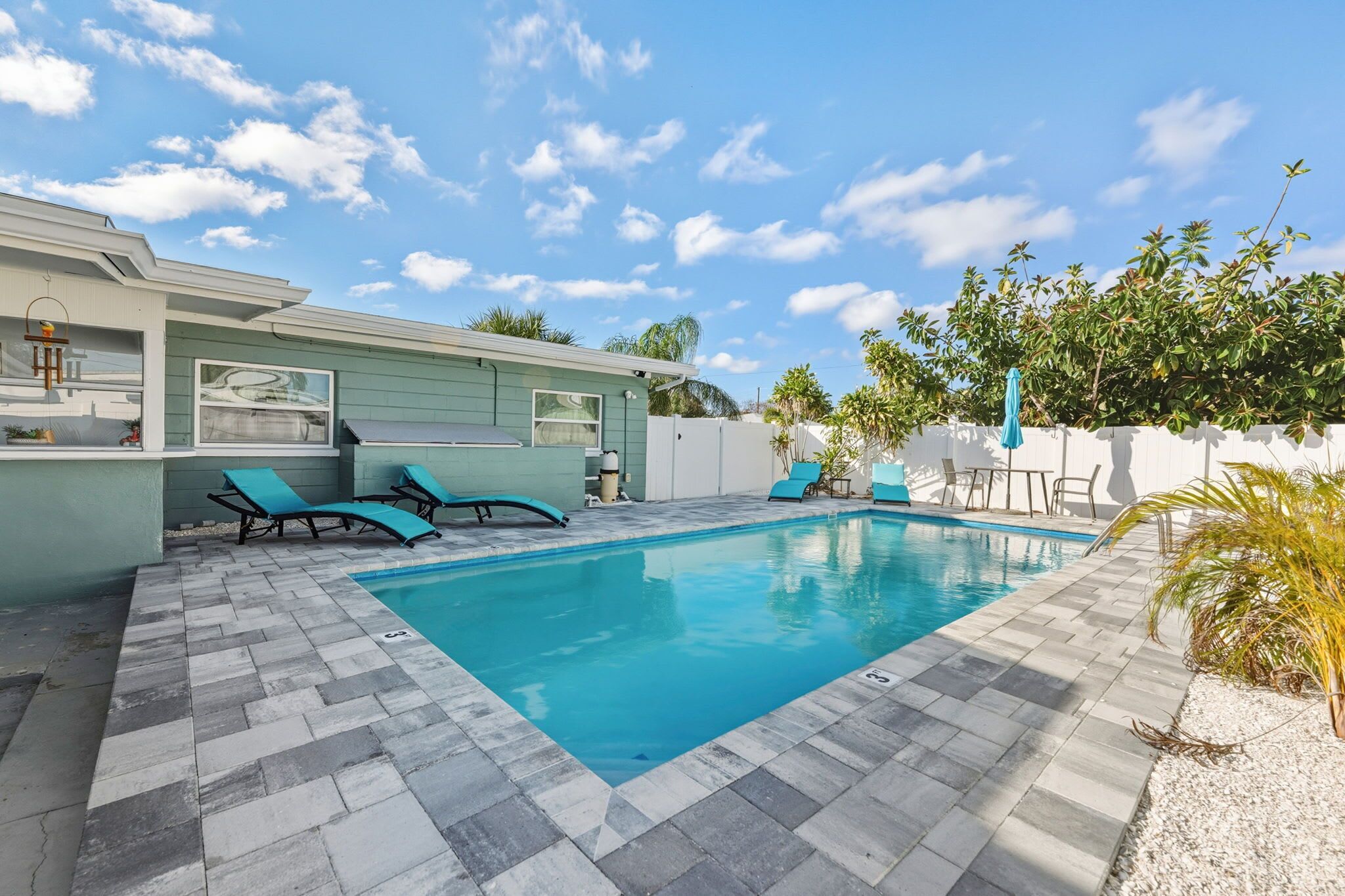 A swimming pool with lounge chairs, a patio area, and a small building with a window.
