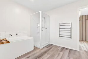 A modern bathroom with a glass-enclosed shower, a white bathtub, and a towel rack. - Roam & Recharge Wanaka - 1BR Luxury Suite (Wānaka)