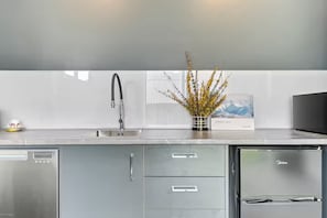 A modern kitchen with stainless steel appliances, a built-in dishwasher, and a vase with yellow flowers on the counter. - Roam & Recharge Wanaka - 1BR Luxury Suite (Wānaka)