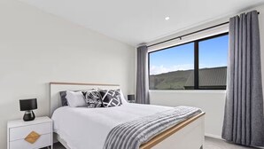 Un dormitorio moderno con una cama grande, una mesita de noche, una lámpara y vistas al exterior a través de una ventana.