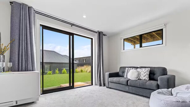 Un salón moderno con un sofá gris, un sillón de peluche gris, un radiador y un ventanal corredero que da a un jardín.