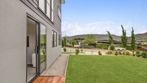 Un edificio moderno con un gran ventanal, una terraza de madera y un césped bien cuidado.