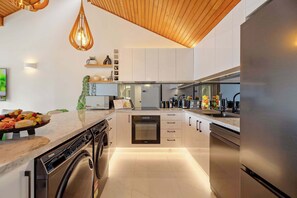 Eine moderne Küche mit integrierter Waschtrockner-Kombination, Edelstahlgeräten und einer Holzbeschichtung an der Decke.