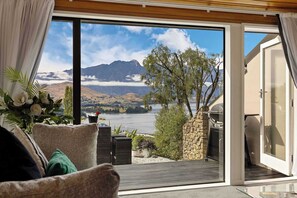 Ein Zimmer mit einer großen Schiebeglasdoor zum Deck mit Blick auf einen See und Berge.