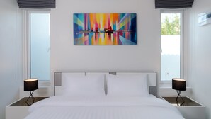 A modern hotel room with a large bed, two bedside tables, a colorful abstract painting, and a window with a view. - Orchid Paradise Homes OPV428 (Hin Lek Fai)