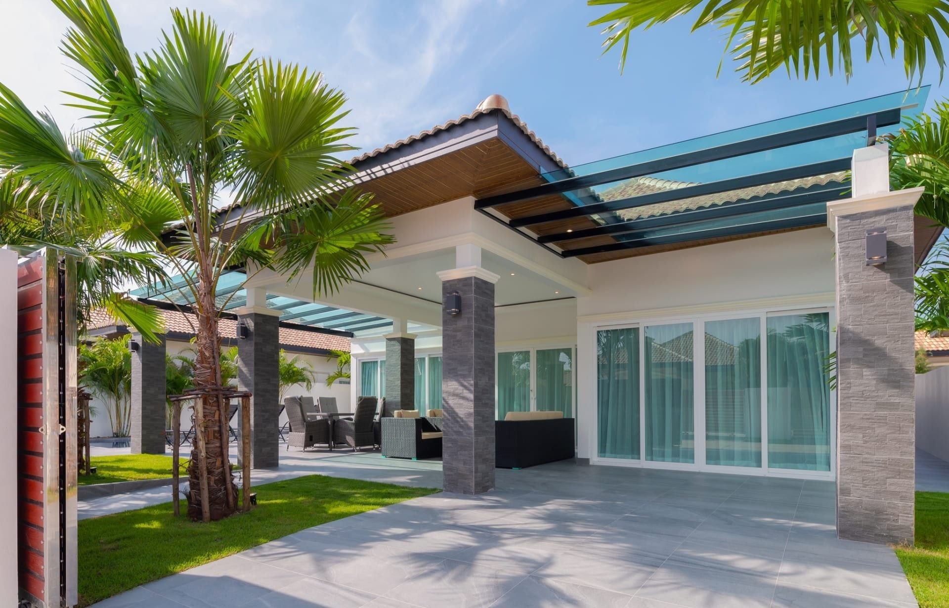 A modern outdoor patio area with a glass ceiling, seating arrangements, and palm trees.