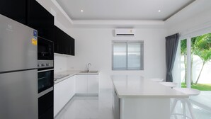 A modern kitchen with a central island, a built-in oven, and a window with blinds. - Orchid Paradise Homes OPV428 (Hin Lek Fai)