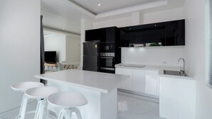 A modern kitchen with a central island, white bar stools, a black refrigerator, and a built-in oven. - Orchid Paradise Homes OPV428 (Hin Lek Fai)