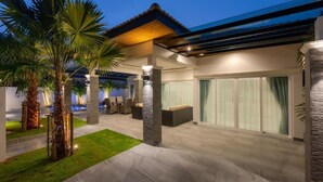 A modern outdoor patio with a covered seating area, palm trees, and a pool. - Orchid Paradise Homes OPV428 (Hin Lek Fai)