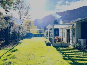 Ein Wohnhaus mit überdachter Terrasse, einem Schornstein, der Rauch abgibt, und einer Bergkulisse im Hintergrund.