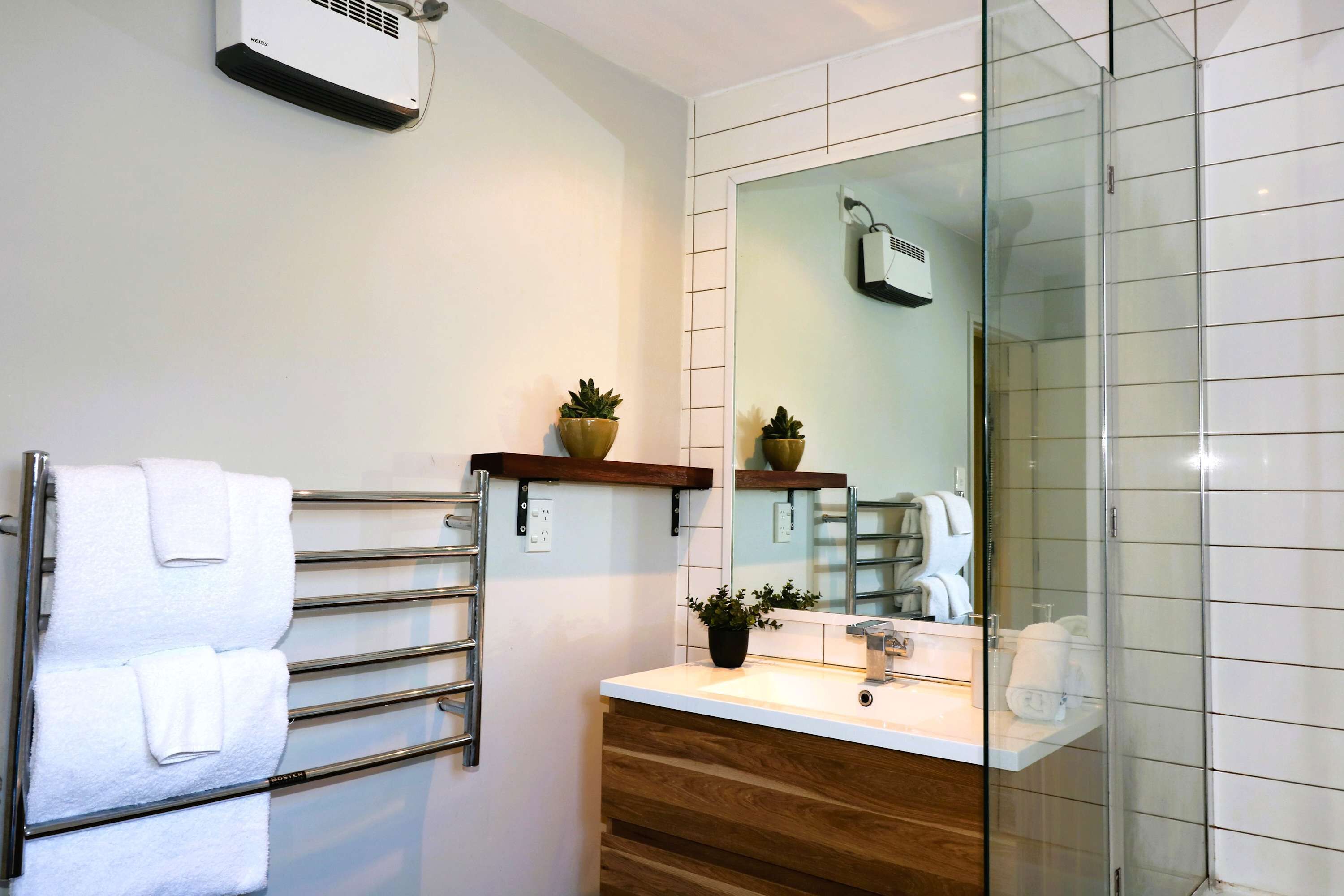 A modern bathroom with a glass shower enclosure, a towel rack with white towels, a wooden vanity with a sink, and a mirror above the vanity.