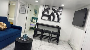 A modern living room with a blue sofa, a black coffee table, a TV, and a painting on the wall. - Adorable 2-br apt Pet-Friendly .Fast WiFi .Near Airport & LIRR (Central Islip)