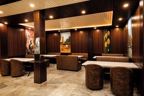 A restaurant with wooden panel walls, cushioned booths, and tables. - Hotel JK Blue Heaven (Varanasi)