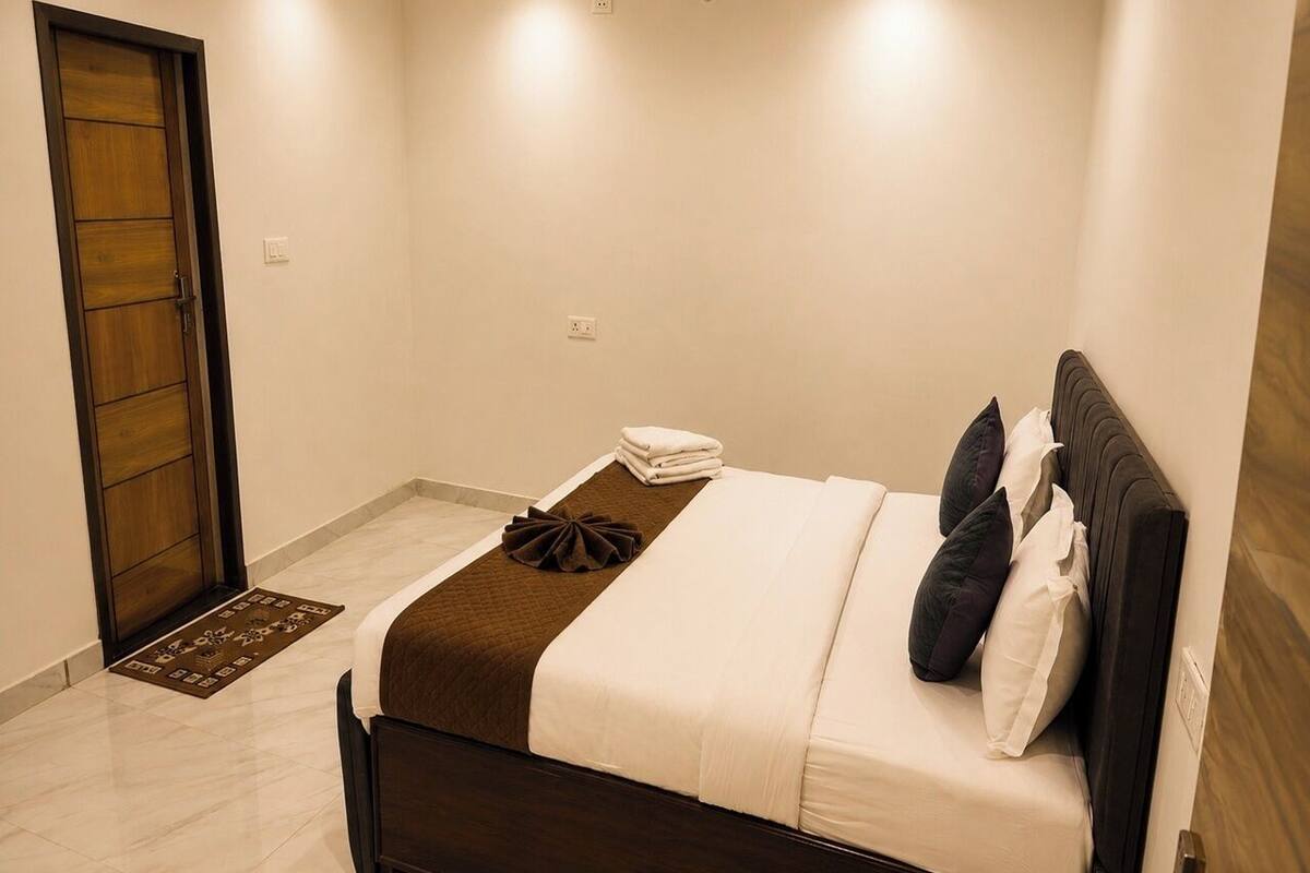 A hotel room with a bed, a wooden door, a small rug, and a wall socket.