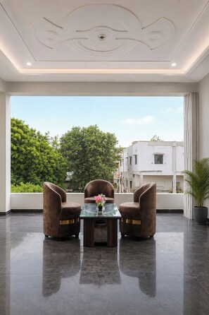 A modern room with a large window, two brown leather chairs, a glass table, and a potted plant. - Hotel JK Blue Heaven (Varanasi)
