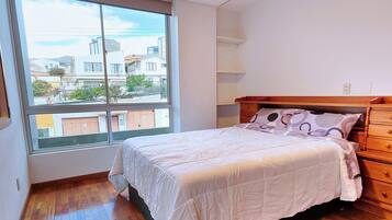Un dormitorio con una cama de madera, un ventanal con vistas a edificios y un piso de madera.