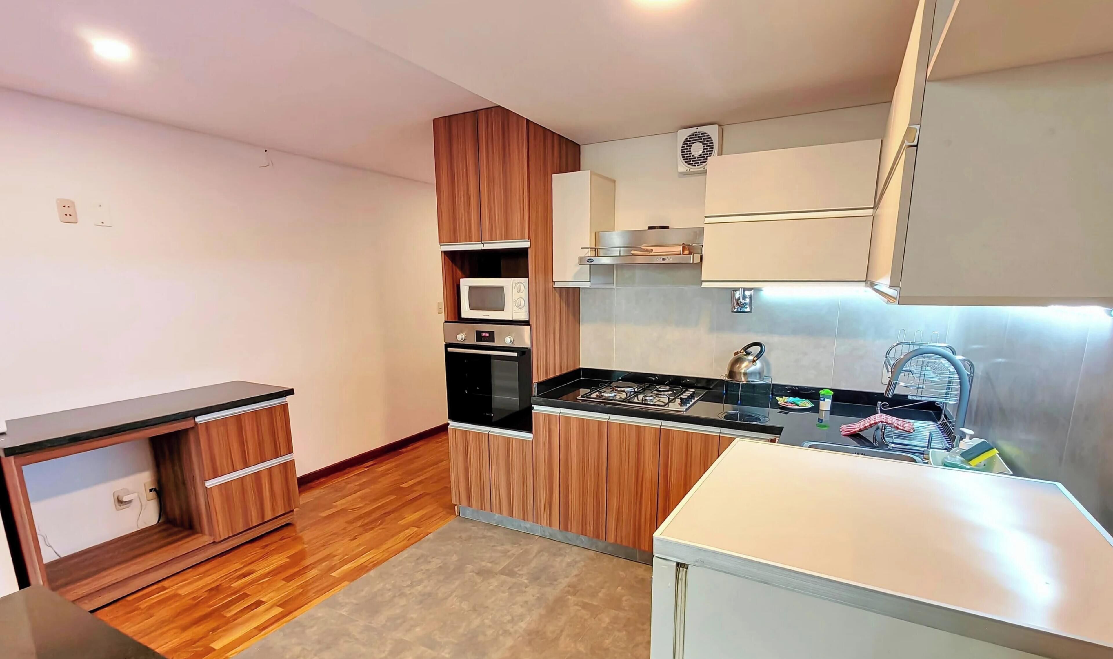 A compact kitchen with wooden cabinets, a microwave, an oven, a gas stove, and a small sink.