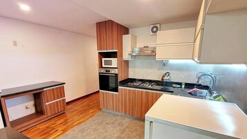 A compact kitchen with wooden cabinets, a microwave, an oven, a gas stove, and a small sink.