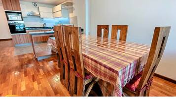 Un comedor con una mesa y sillas de madera, una cocina al fondo y un piso con patrón de espiga.